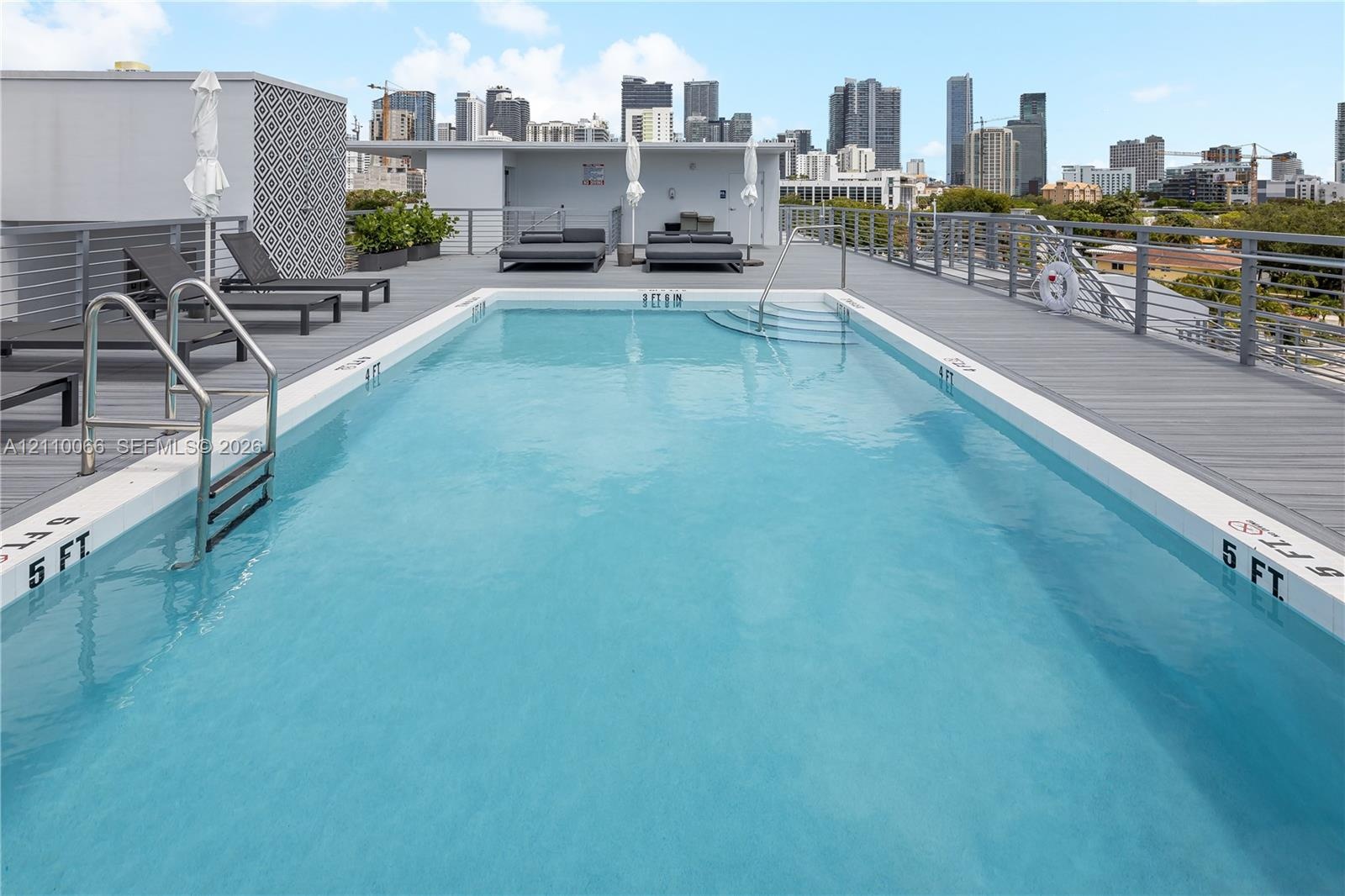 Rooftop swimming pool featuring gray composite decking, integrated metal railings, and built-in steps