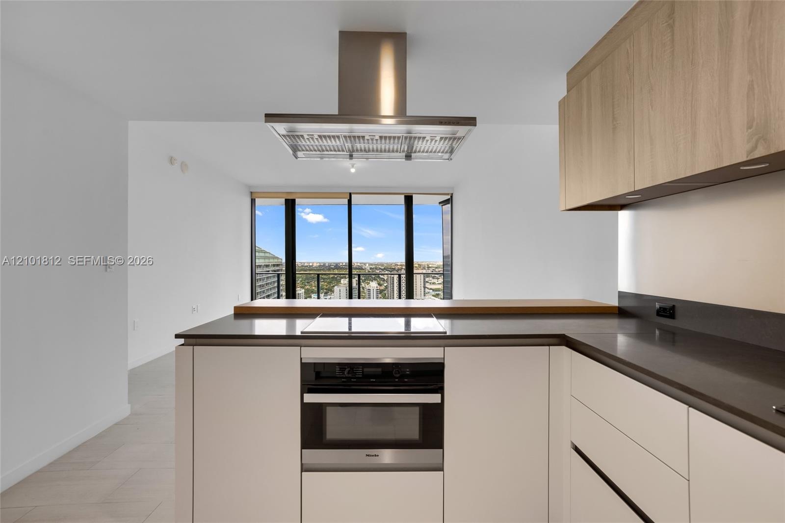 Contemporary kitchen featuring light wood-finish upper cabinetry, integrated stainless steel appliances, dark stone-finish countertops, a wood-topped 
