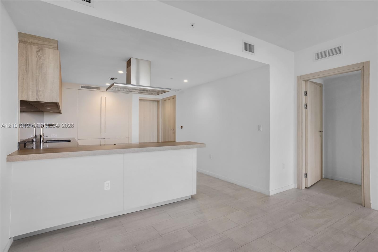 Kitchen featuring flat-panel light wood cabinetry, integrated appliances, stainless steel range hood, breakfast bar, and tile flooring