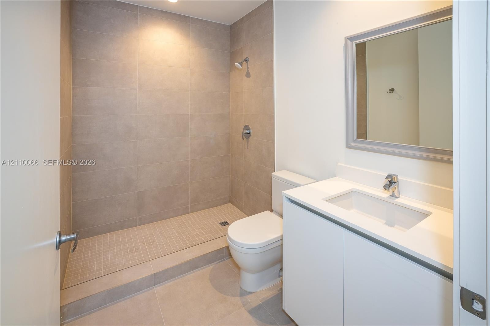 Bathroom featuring a walk-in shower with large-format wall tile, a white vanity with an integrated sink, a rectangular framed mirror, and chrome plumb