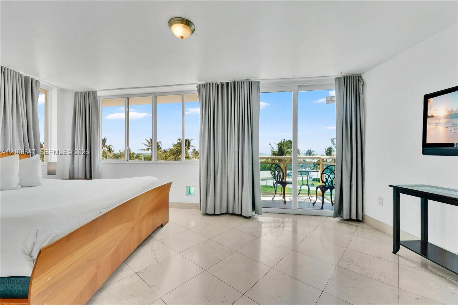 Light-colored stone tile flooring, expansive wall-to-wall glass windows, and sliding glass doors with access to an exterior balcony