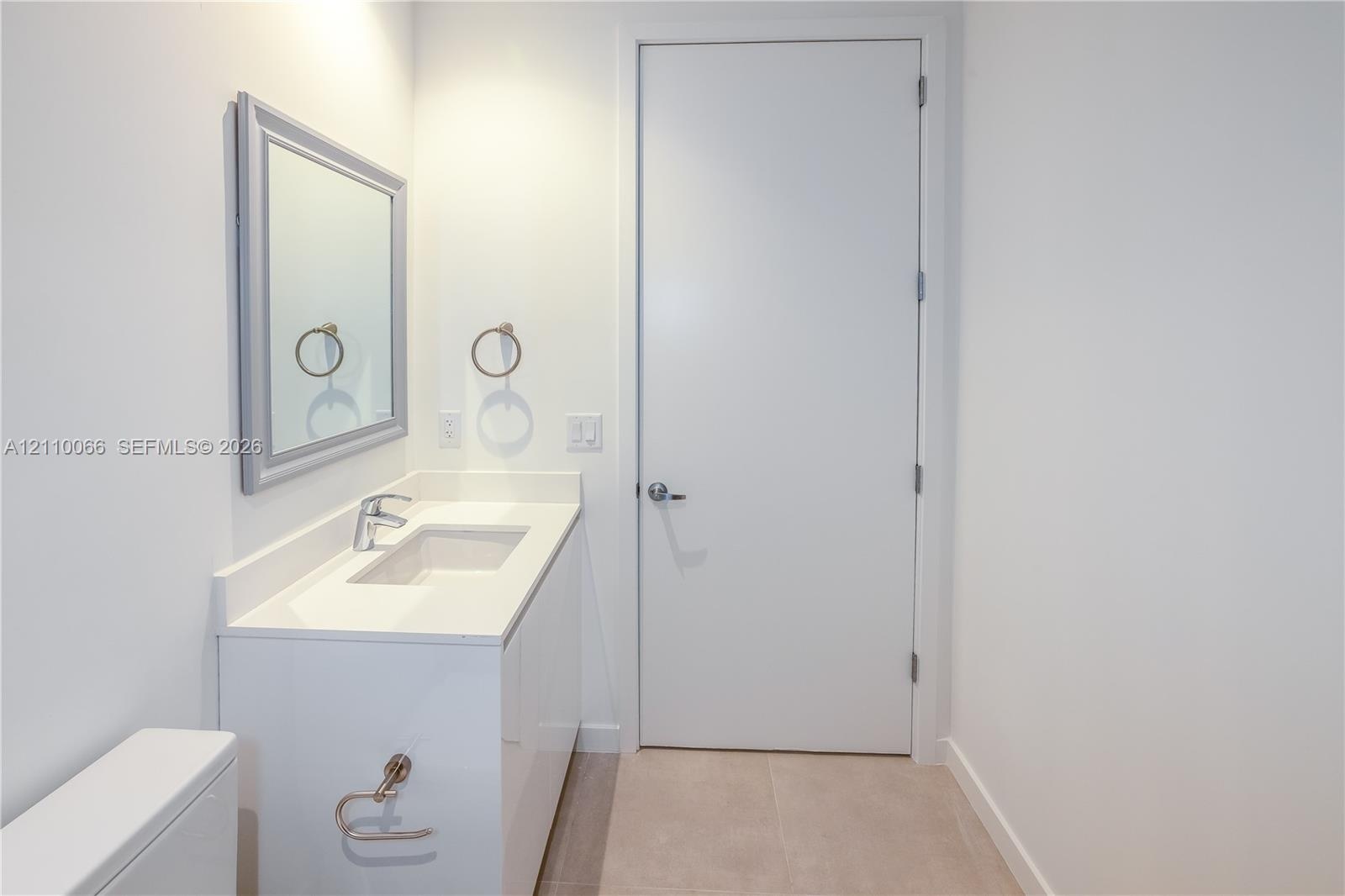 Bathroom featuring a white vanity cabinet with a solid surface countertop, an integrated rectangular sink, a framed wall-mounted mirror, and tile floo