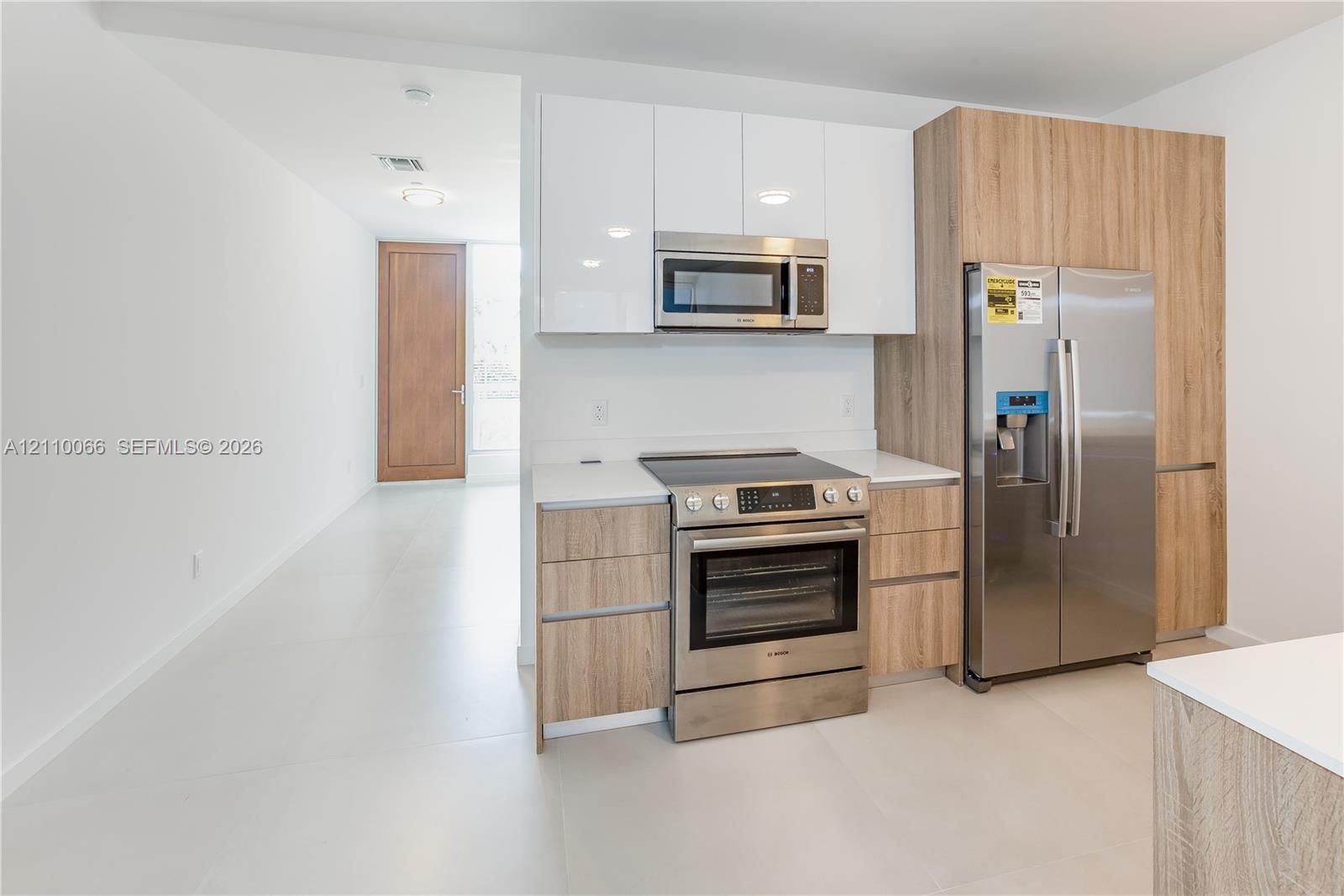 Kitchen featuring two-tone cabinetry with gloss white upper units, wood-finish lower cabinetry, integrated stainless steel appliances, solid-surface c