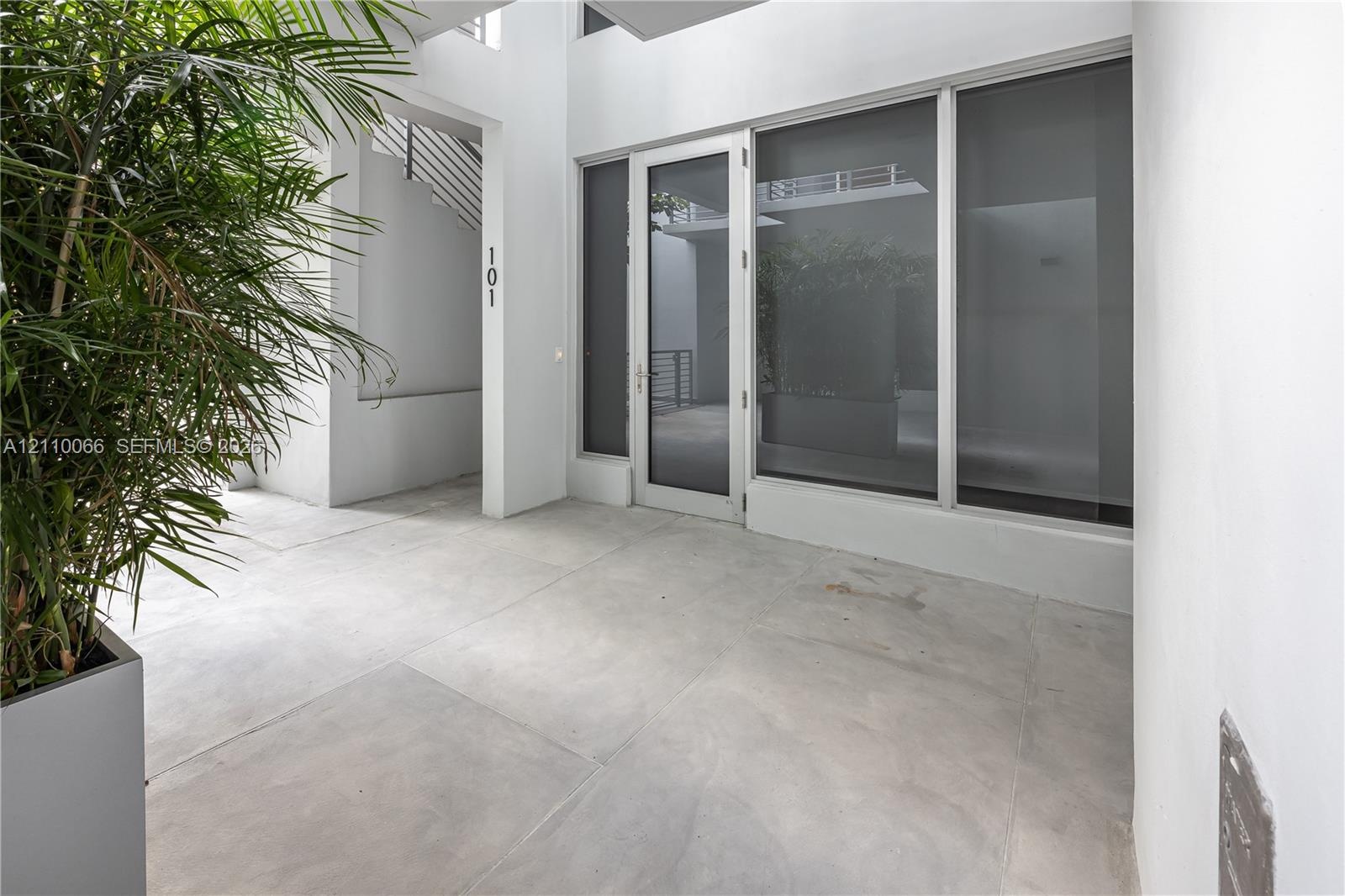 Covered entryway featuring large-format concrete flooring, floor-to-ceiling glass paneling, a full-lite glass entry door, and white stucco walls