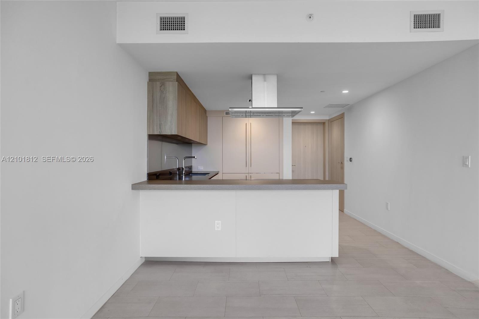 Kitchen featuring a peninsula with solid-surface countertop, wood-finish cabinetry, stainless steel island range hood, and tile flooring