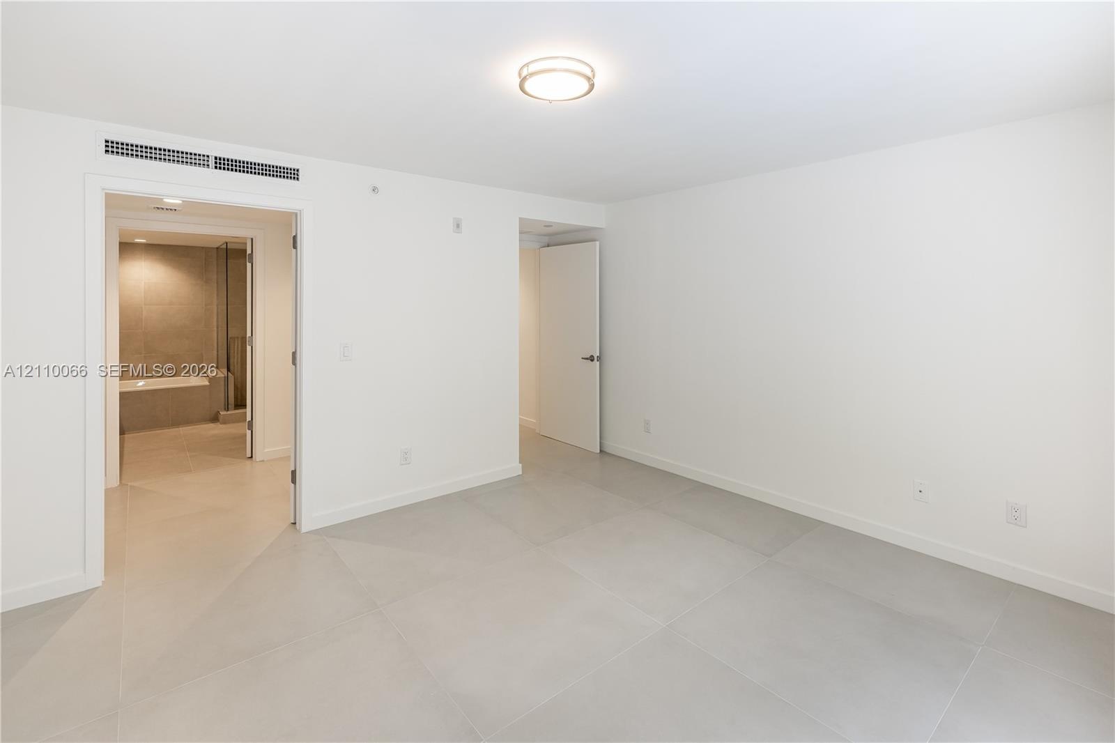 Neutral interior space featuring large-format light-toned tile flooring, minimalist white walls, recessed ceiling lighting, and solid-core interior do
