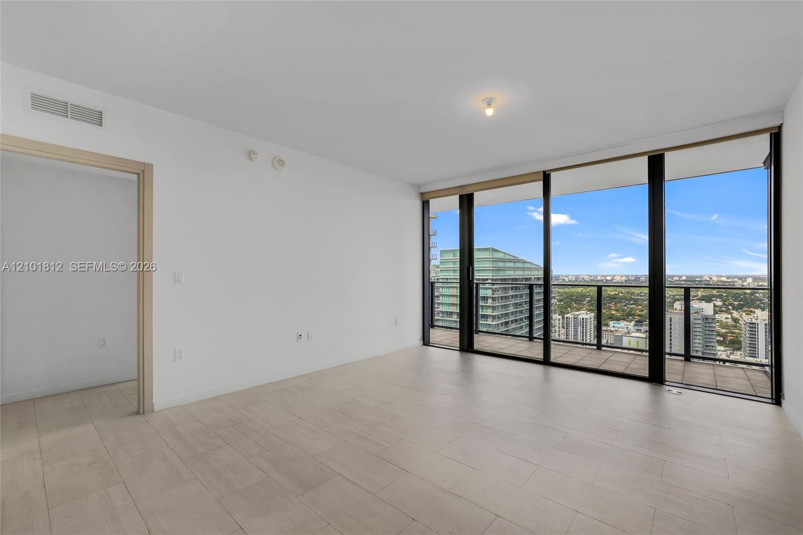 Open-concept interior featuring floor-to-ceiling glass wall, private balcony with metal railing, and neutral wood-finish flooring