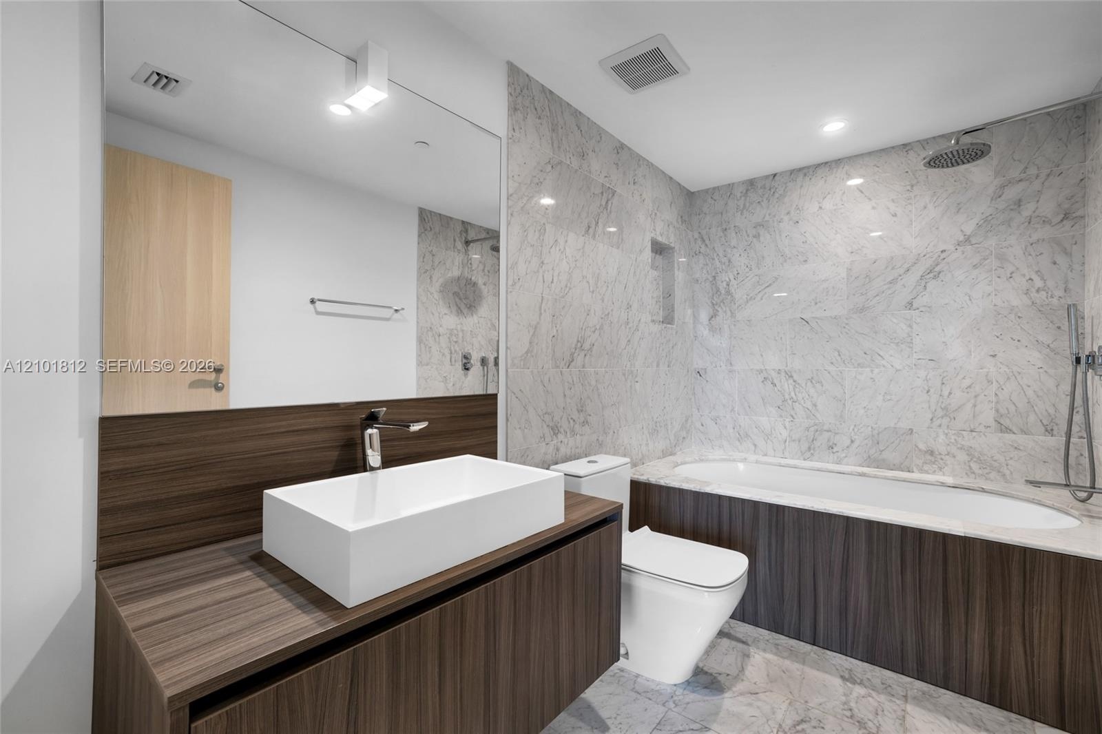 Contemporary bathroom featuring a floating wood-finish vanity with a rectangular white vessel sink, stone-look countertop, and chrome wall-mounted fau