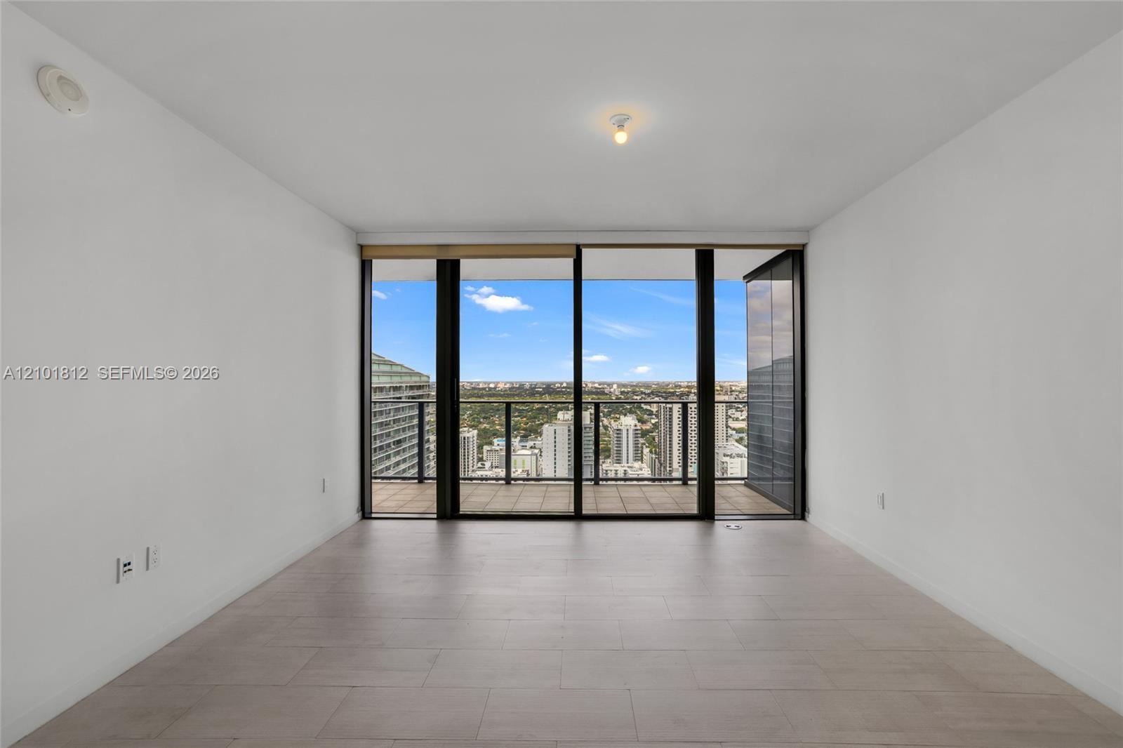 Floor-to-ceiling sliding glass doors, private balcony with metal railing, and neutral tile flooring