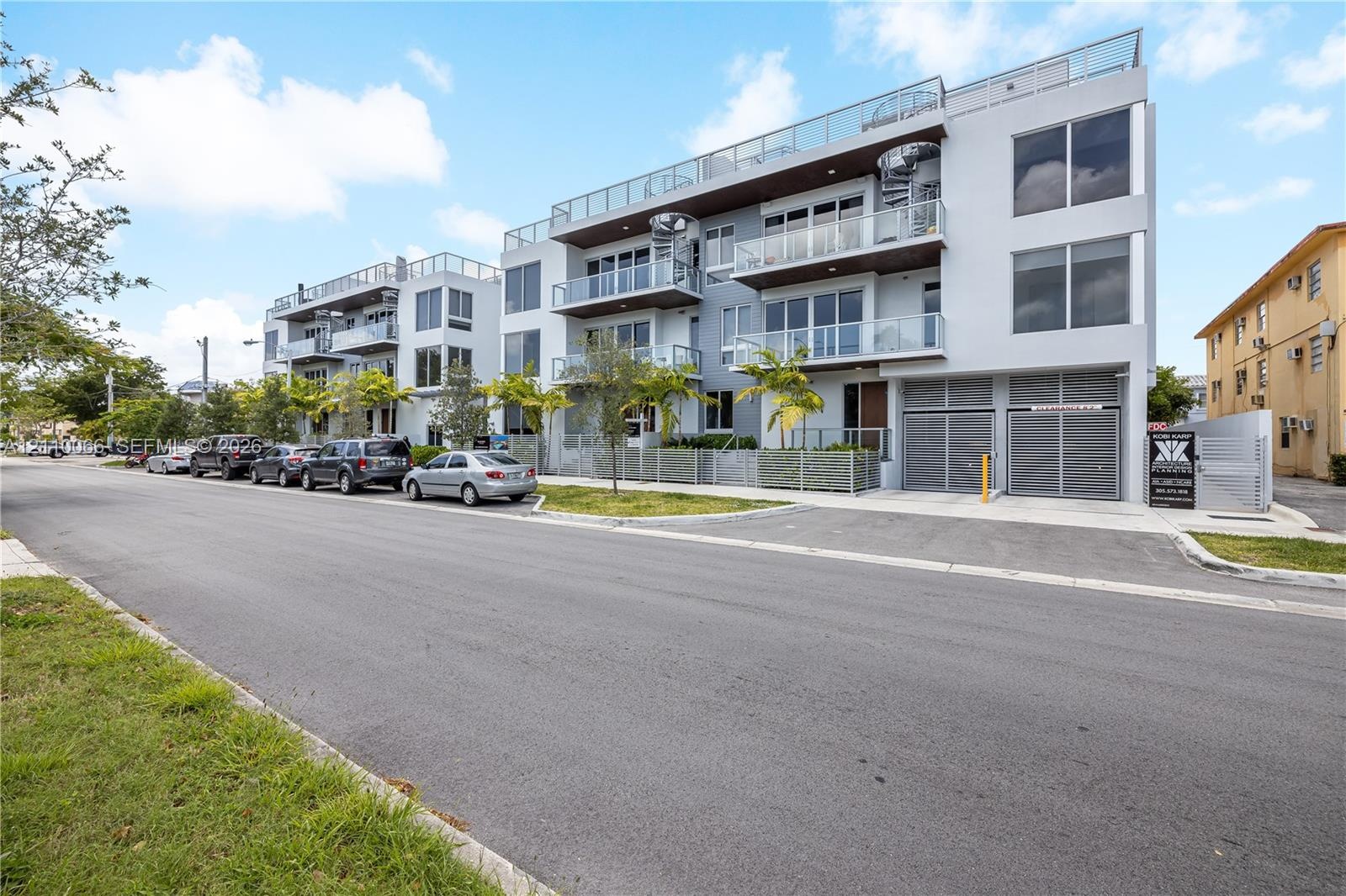 Modern multi-story residential building featuring a smooth stucco facade, glass-paneled balconies, rooftop terraces, spiral staircase architectural el