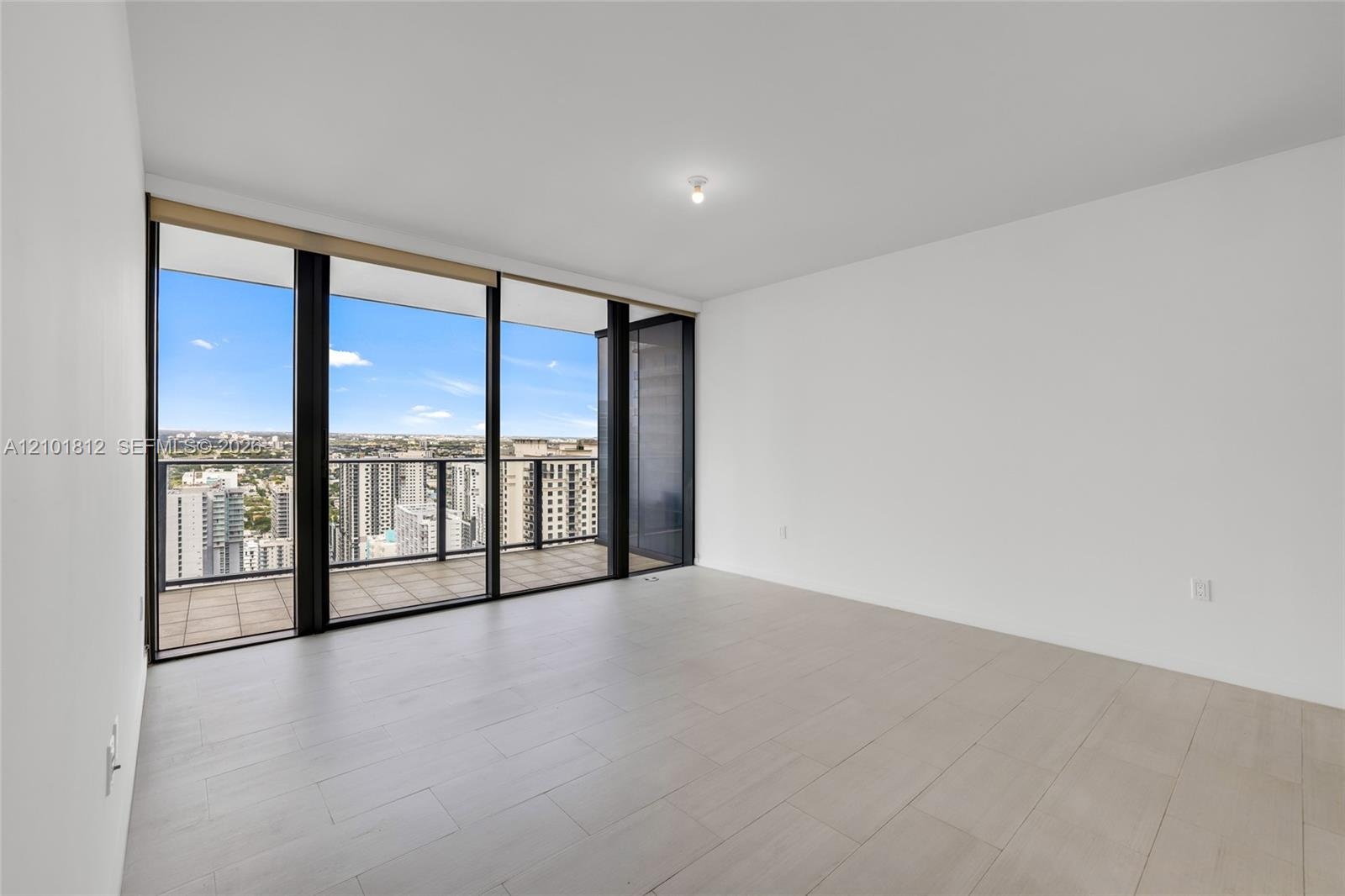Open interior space featuring light-toned tile flooring, floor-to-ceiling windows, and a tiled private balcony with glass railing