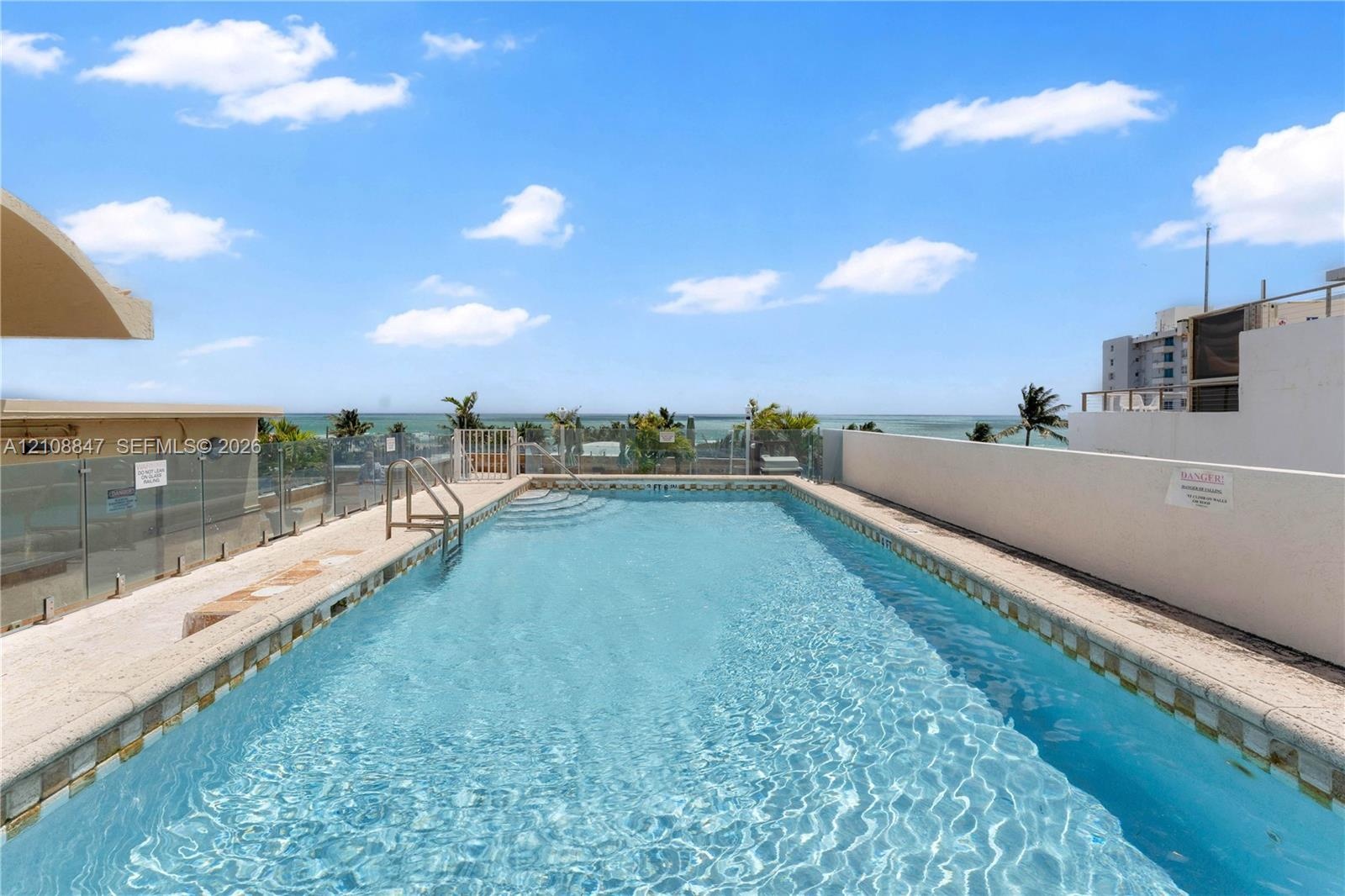 Rooftop swimming pool featuring stone-style decking, a metal ladder, and glass panel railing