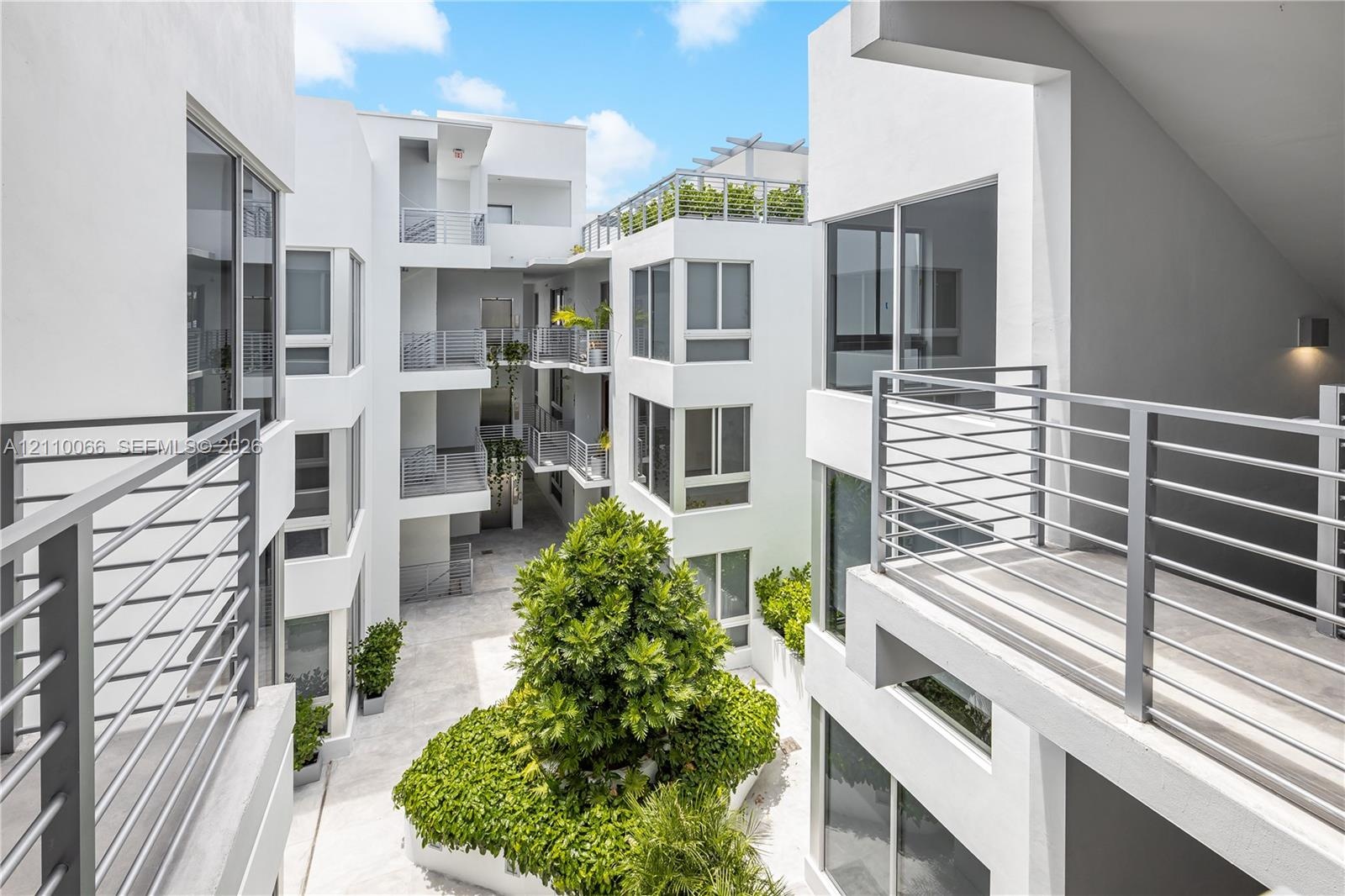 Modern multi-story structure featuring a smooth white stucco facade, tiered metal railings, expansive glass windows, and an open-air central courtyard