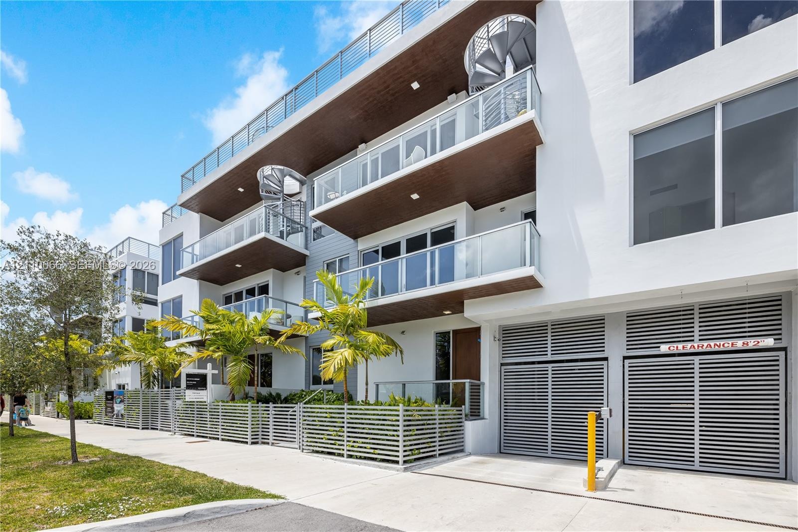 Modern multi-level exterior featuring white stucco cladding, integrated wood-finish balcony ceilings, glass railings, metal spiral staircases, and lou