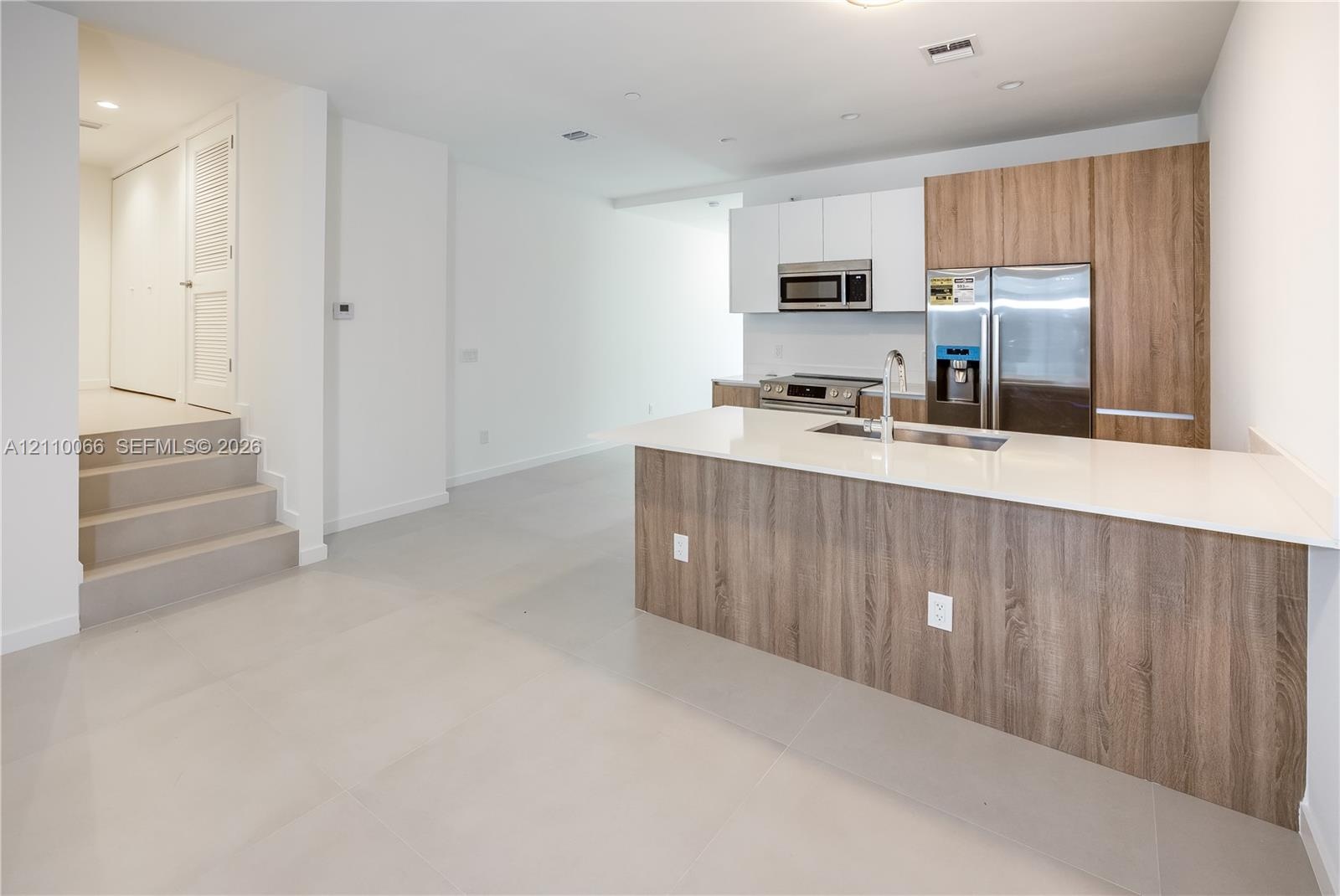 Kitchen featuring dual-tone cabinetry with wood-finish and matte white uppers, quartz countertops, a central island, stainless steel appliances, and l