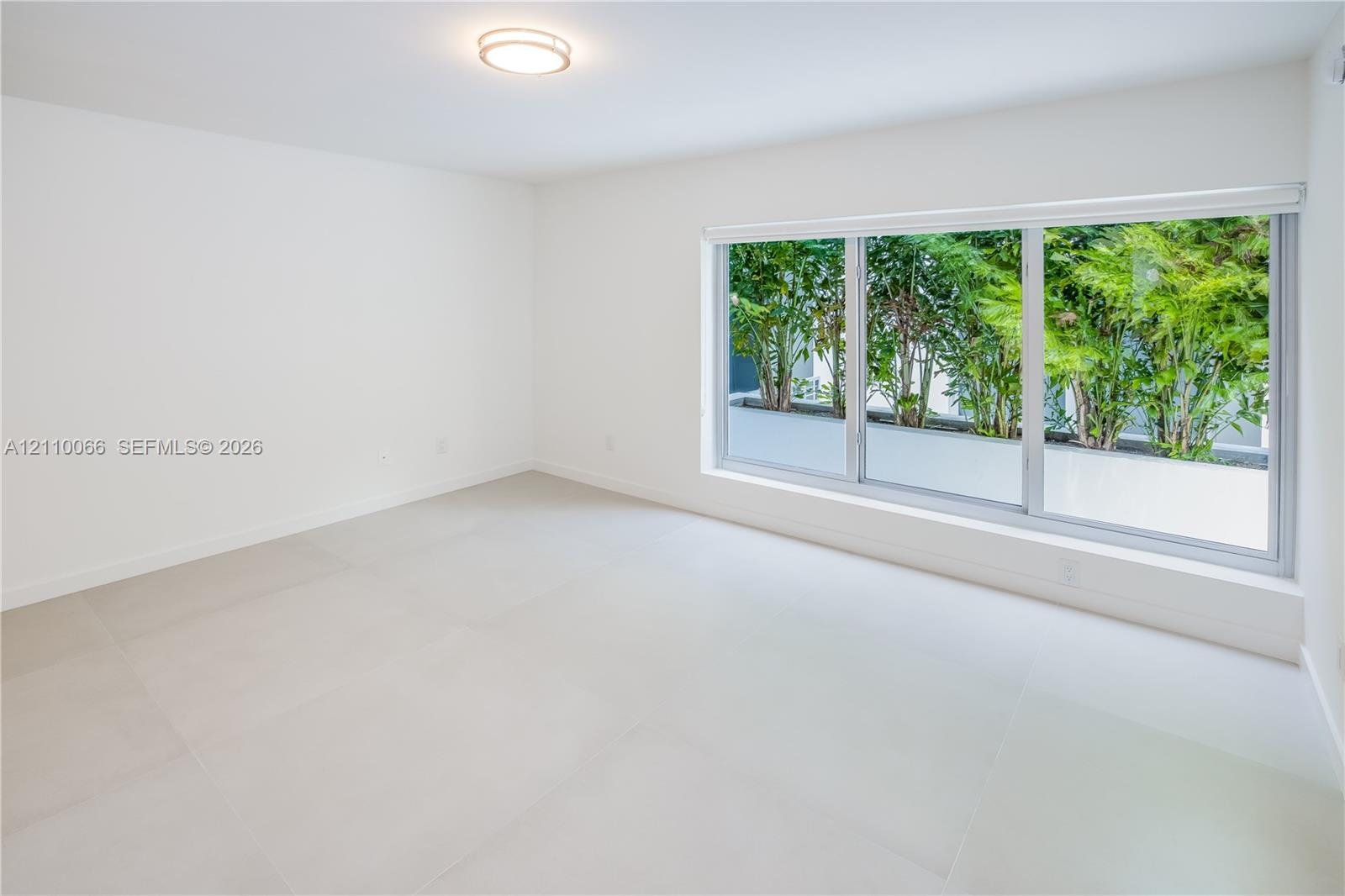 Neutral-toned tile flooring, large three-pane picture window, recessed ceiling lighting, and exterior greenery