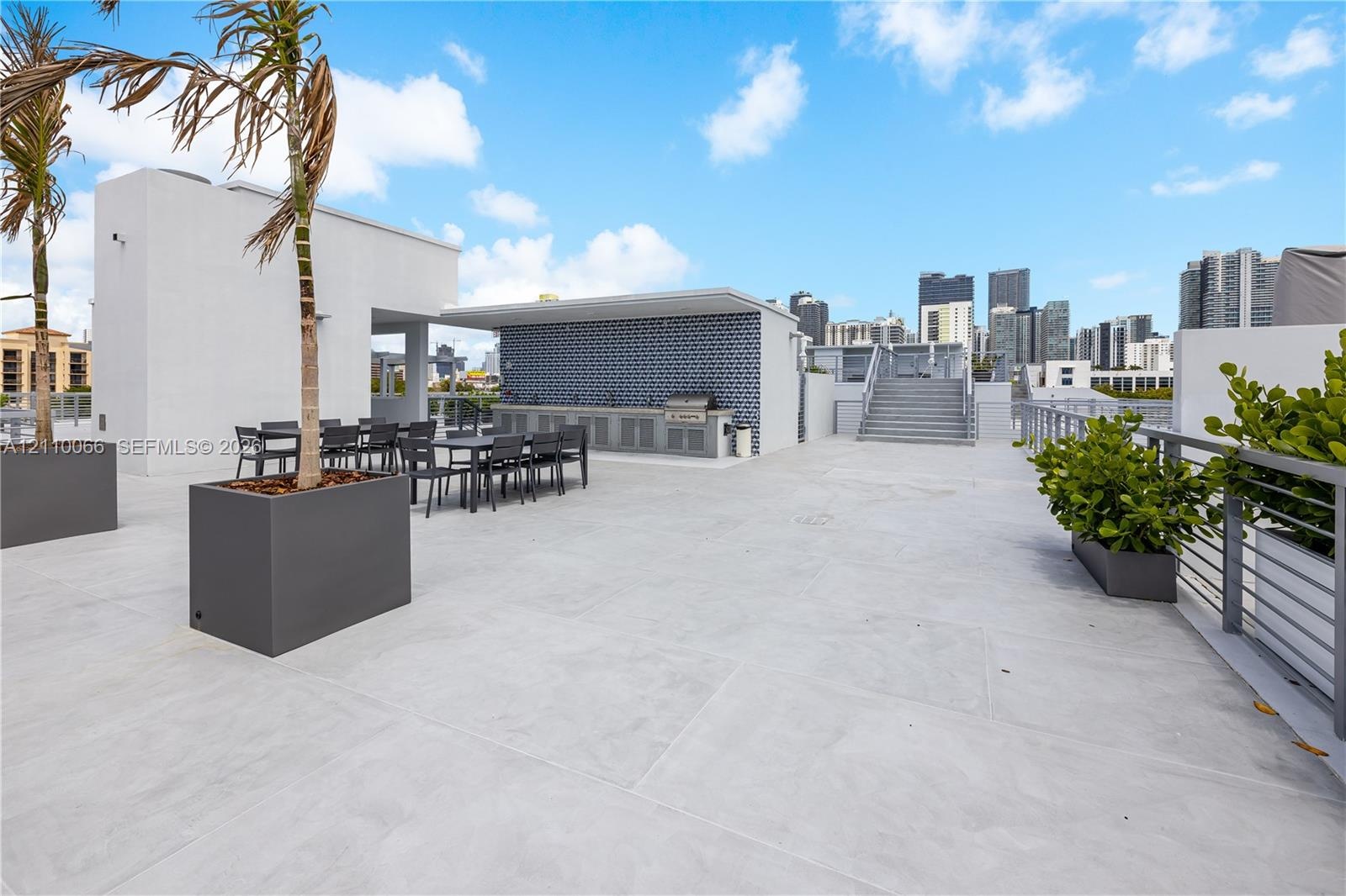 Expansive rooftop terrace featuring concrete flooring, a built-in outdoor kitchen with patterned tile backsplash, metal railings, and integrated plant