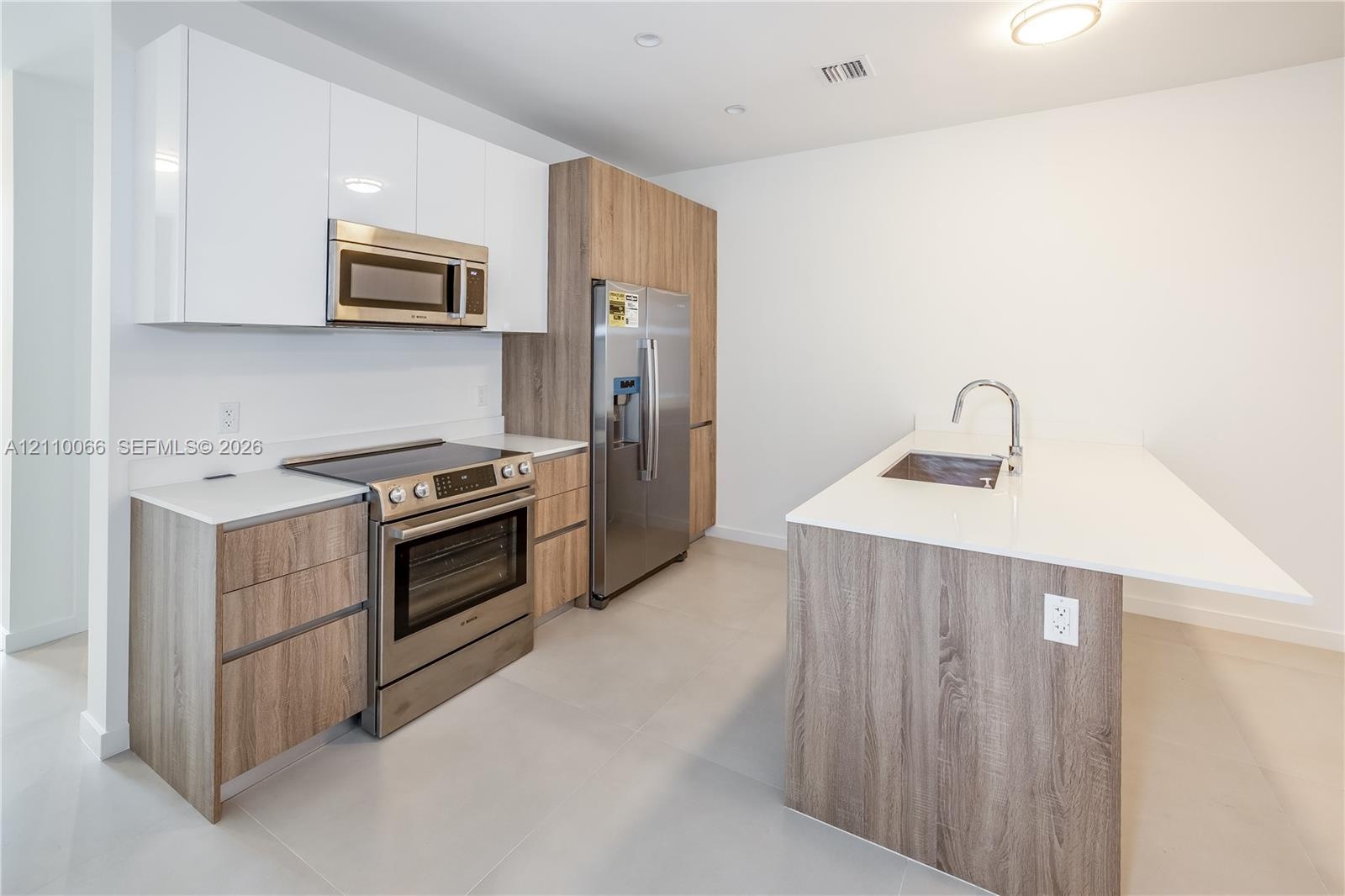 Kitchen featuring white gloss upper cabinetry, wood-finish lower cabinetry, a stainless steel appliance suite, stone-surface countertops, and a centra