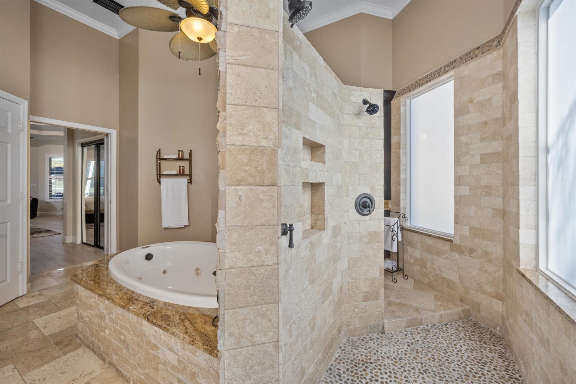 Bathroom featuring a jetted soaking tub with a stone-finished deck, walk-in shower with natural stone tile walls, pebble floor inlay, and recessed wal