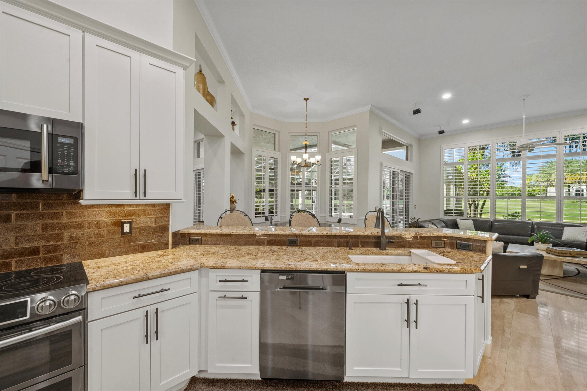 Kitchen featuring white shaker-style cabinetry, stone countertops, brick-tile backsplash, stainless steel appliances, and tile flooring