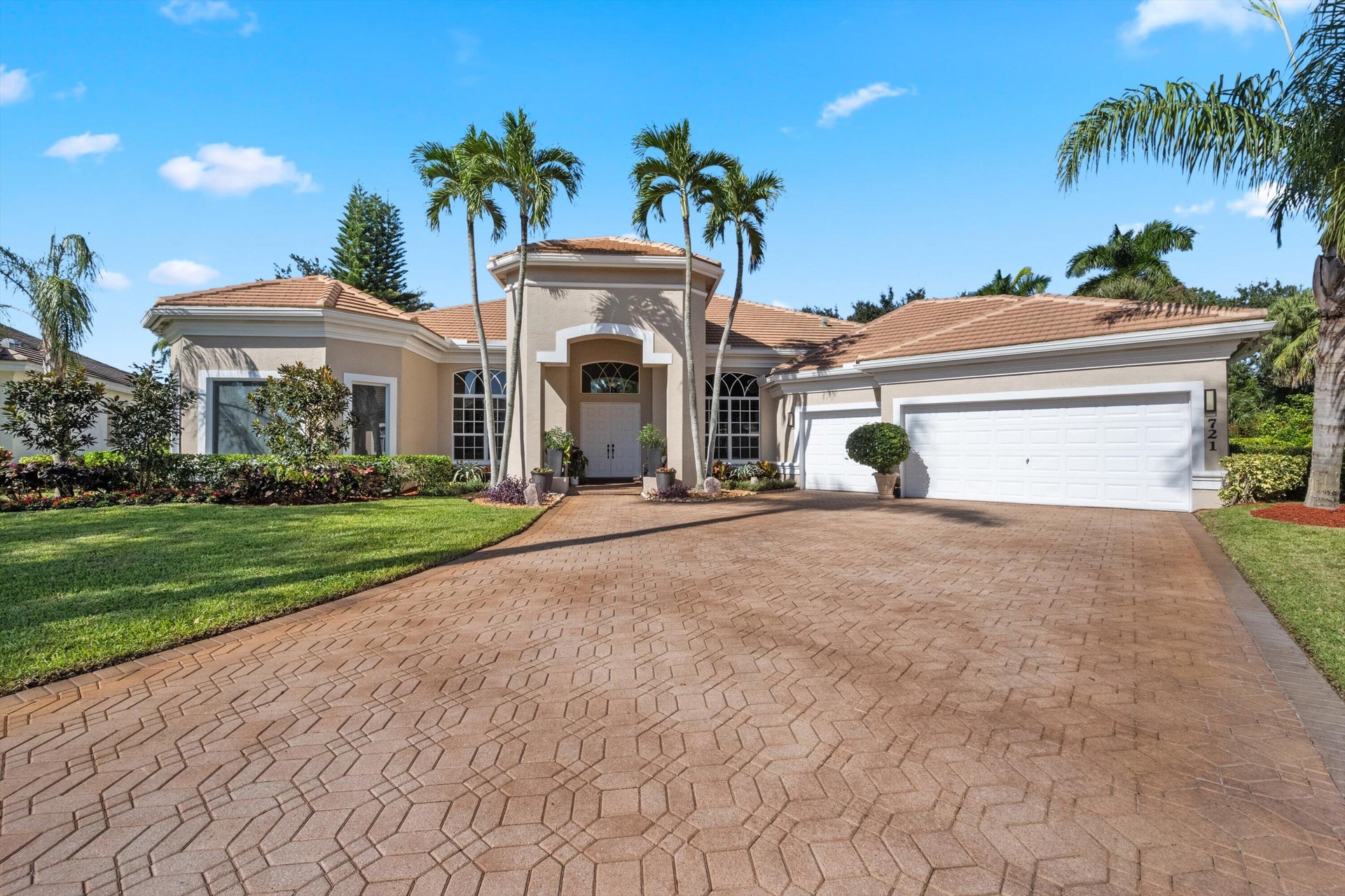 Single-story residence featuring a tile roof, stucco exterior, arched entryway, stamped concrete driveway, and established palm landscaping