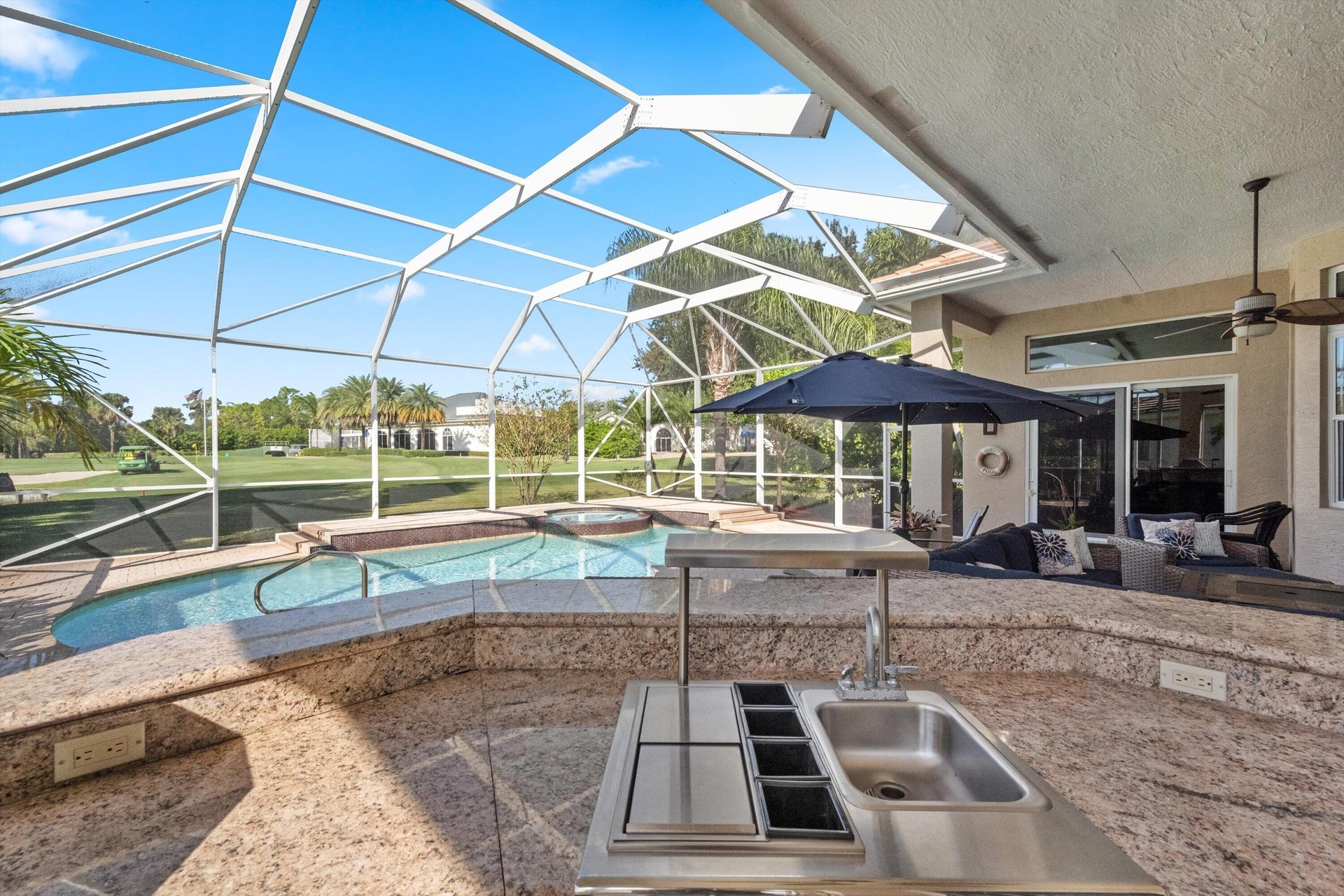 Screened outdoor living area featuring a custom pool, integrated spa, built-in stone-surfaced kitchen island with stainless steel sink, and overhead c