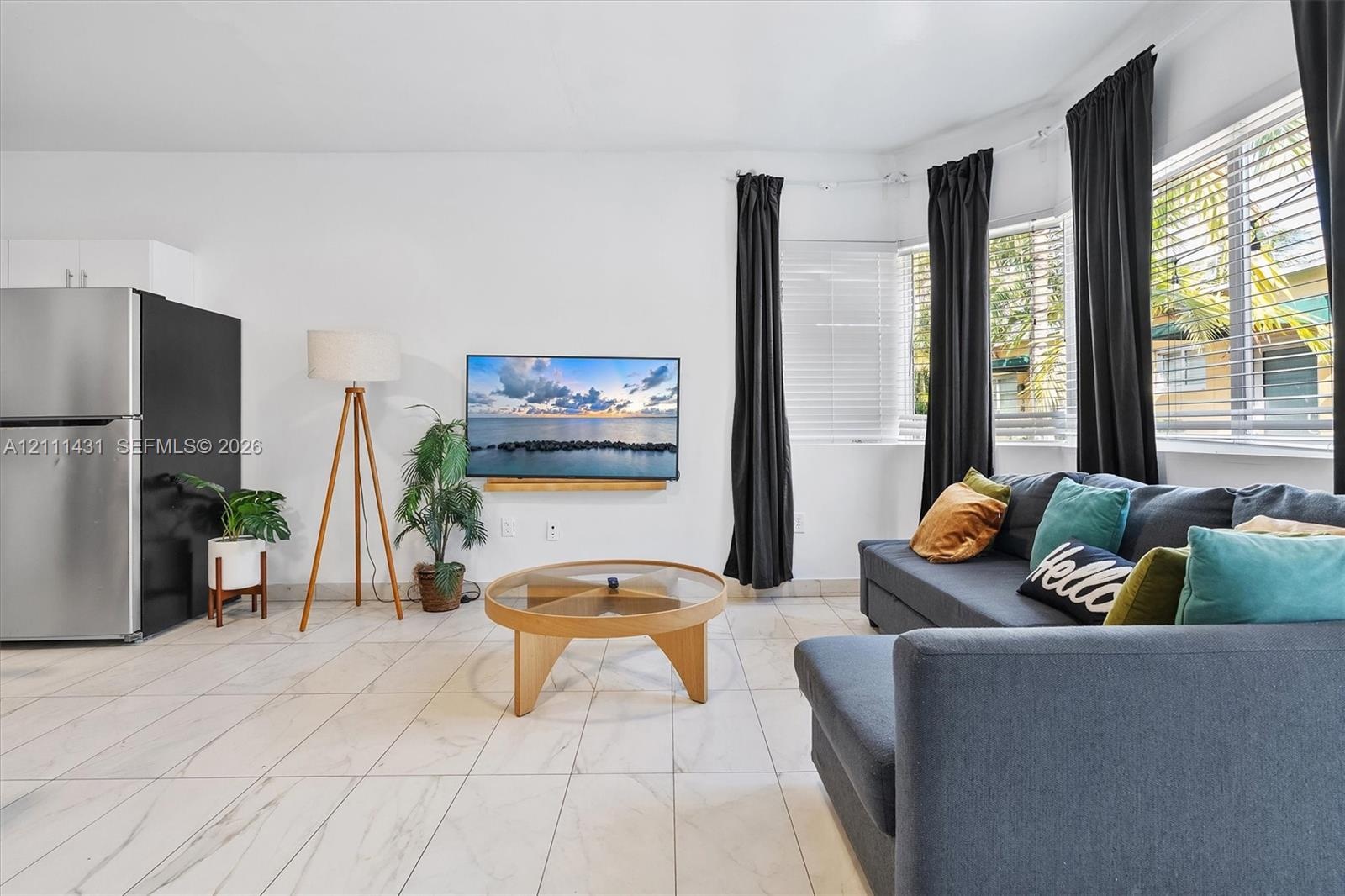 Open-concept area featuring light-toned tile flooring, recessed window bay, and stainless steel refrigerator
