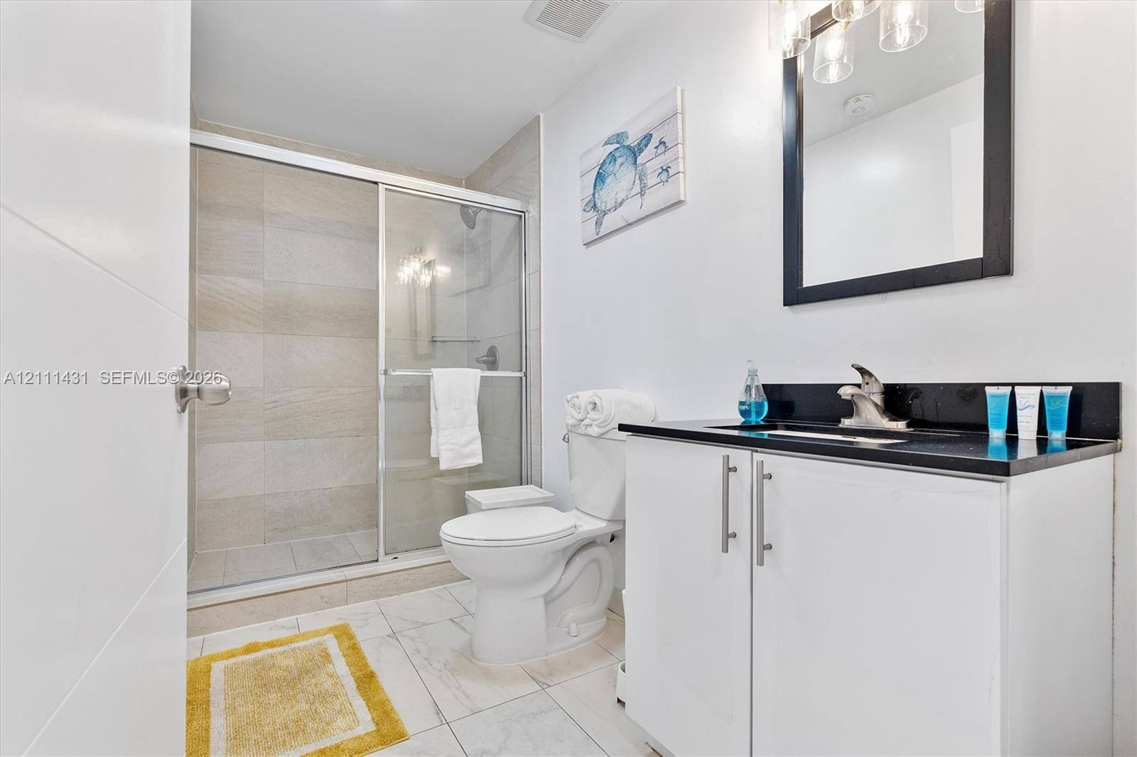 Bathroom featuring a white vanity cabinet with a dark stone countertop, an integrated sink, a framed mirror with integrated lighting, and a walk-in sh