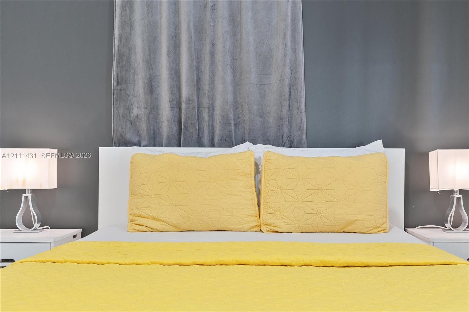 Bedroom featuring a charcoal accent wall, a white headboard with yellow bedding, and matching bedside lamps