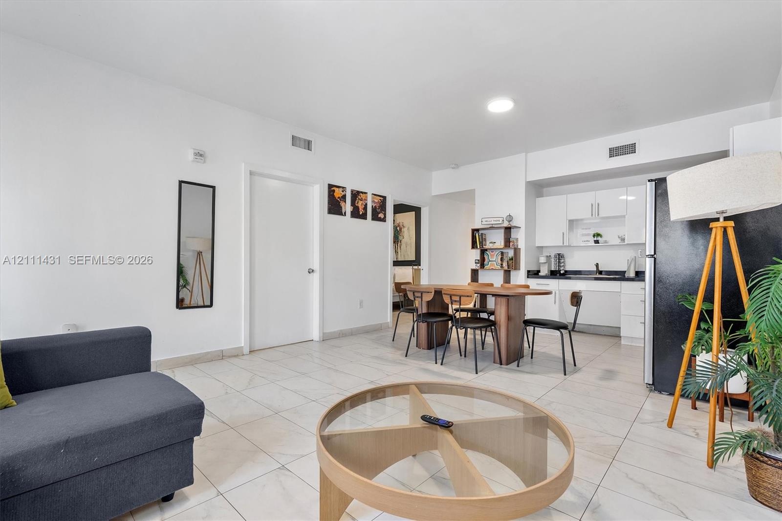 Open living area featuring large-format stone-style tile flooring, white cabinetry with contrasting black countertops, and recessed lighting
