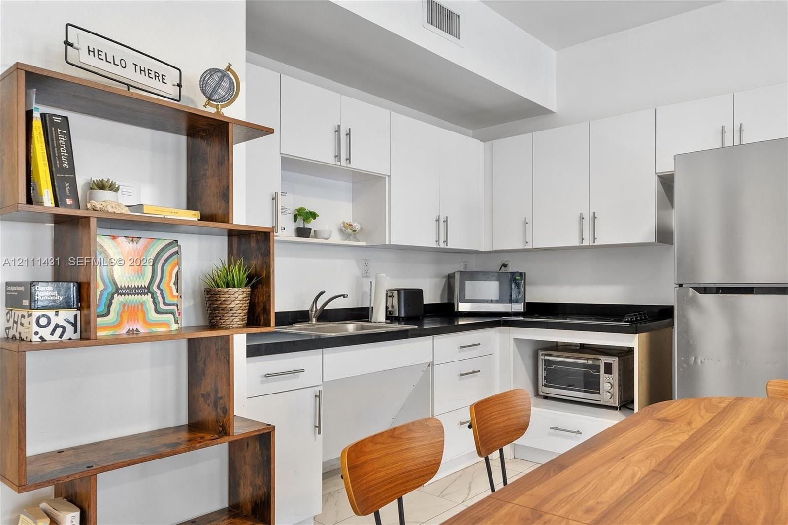Kitchen featuring white cabinetry, contrasting dark stone countertops, stainless steel refrigerator, undermount sink with a gooseneck faucet, and ligh