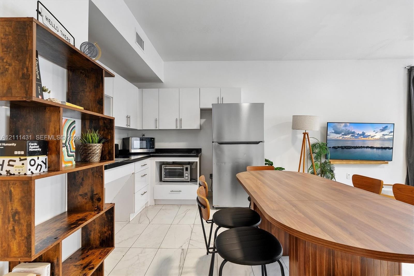 Kitchen featuring white flat-panel cabinetry, contrasting dark countertops, stainless steel refrigerator, and tile flooring