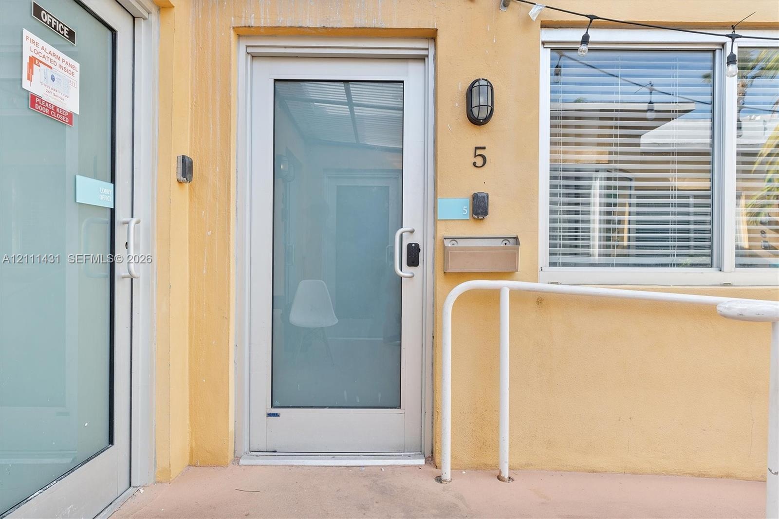 Full-glass entry door with metallic frame, wall-mounted exterior sconce, brushed metal mailbox, and aluminum handrail