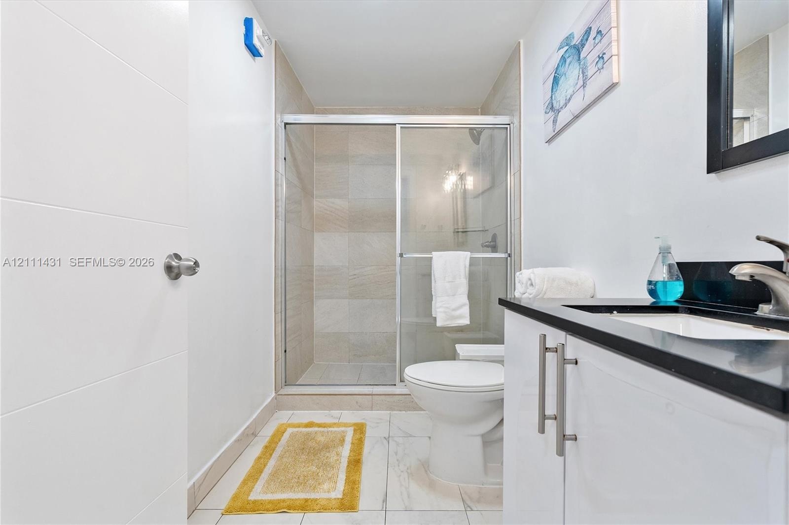 Bathroom featuring a vanity with a dark stone countertop, a walk-in shower with sliding glass doors and neutral-toned wall tile, and light-toned tile 