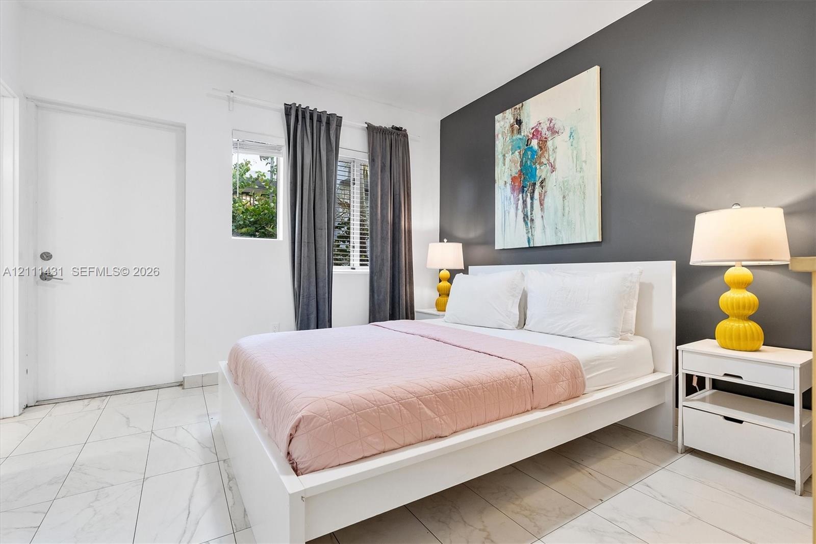 Bedroom featuring large-format tile flooring, a charcoal accent wall, and a window with horizontal blinds