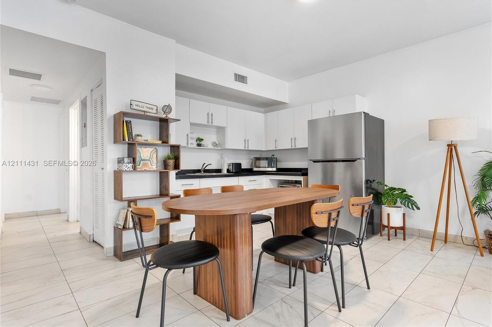 Kitchen featuring white shaker-style cabinetry, black stone countertops, stainless steel refrigerator, and light-toned tile flooring