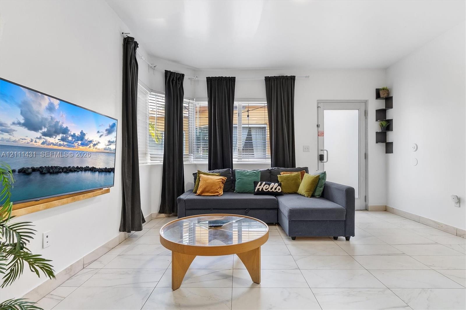 Living area featuring large format tile flooring, a multi-paneled bay window, a built-in wooden media shelf, and a glass-paned exterior door