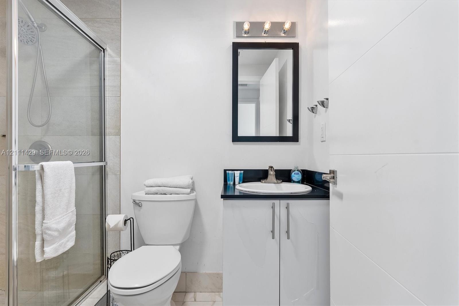 Bathroom featuring a shower with sliding glass doors, a vanity with a dark countertop and white cabinetry, an integrated sink, and a rectangular mirro