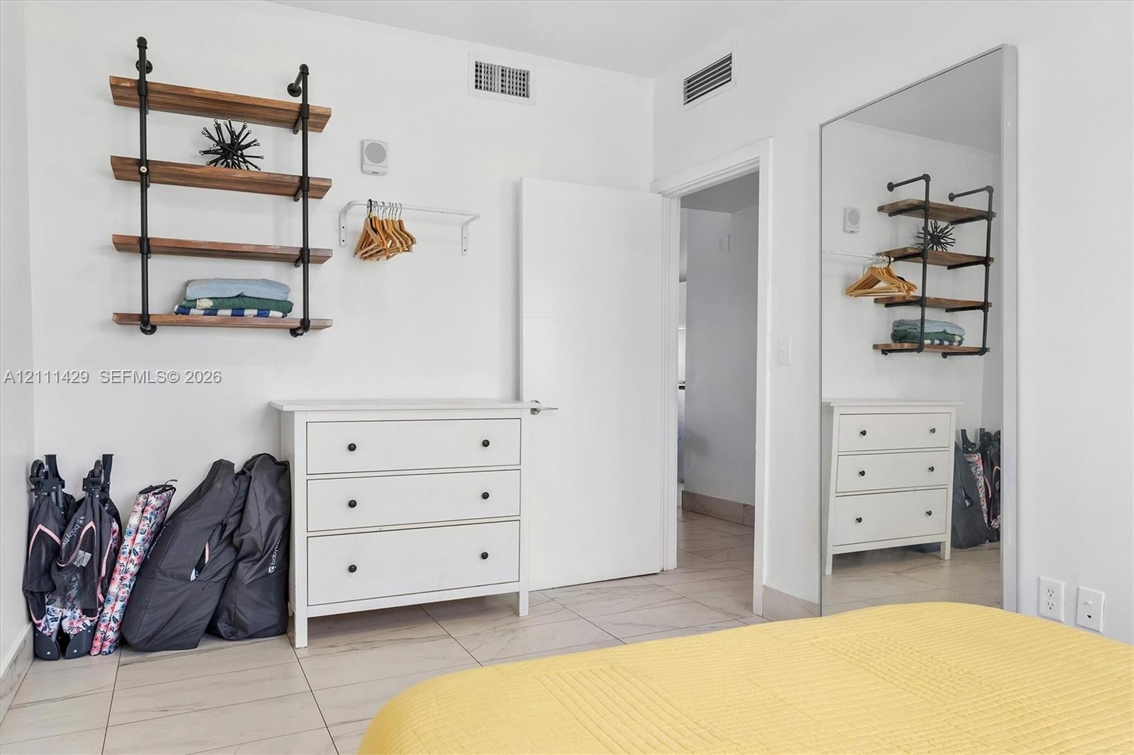 Wall-mounted industrial-style shelving with wood-finish planks, white tile flooring, and a floor-to-ceiling mirror