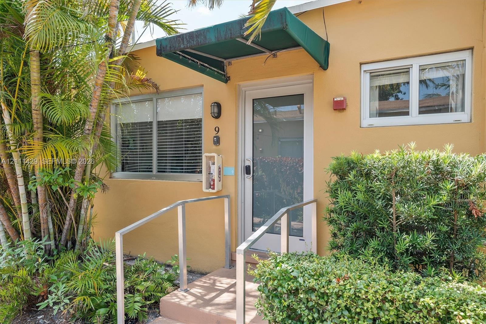 Exterior entrance featuring a concrete stoop with metal handrails, a glass-panel entry door, an integrated green fabric awning, and dual-pane windows