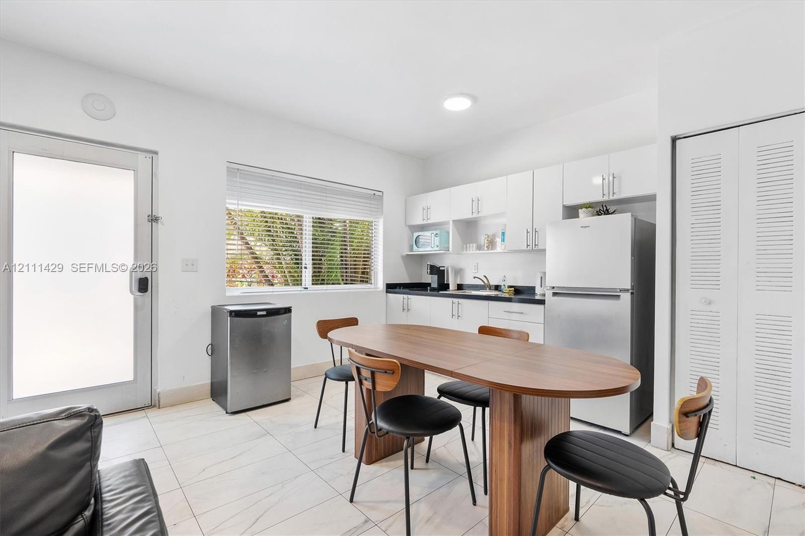 Kitchenette featuring white cabinetry, contrasting dark countertops, a stainless steel refrigerator, white tile flooring and a closet with louvered do