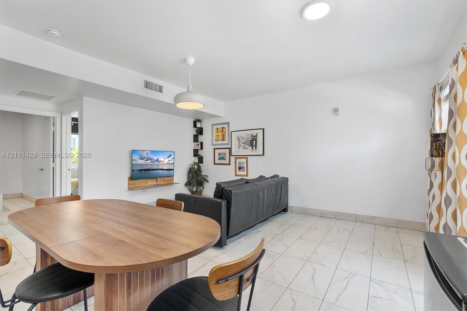 Open-concept interior featuring light-toned tile flooring, recessed ceiling lighting, a modern dome pendant fixture, and a wall-mounted floating shelf