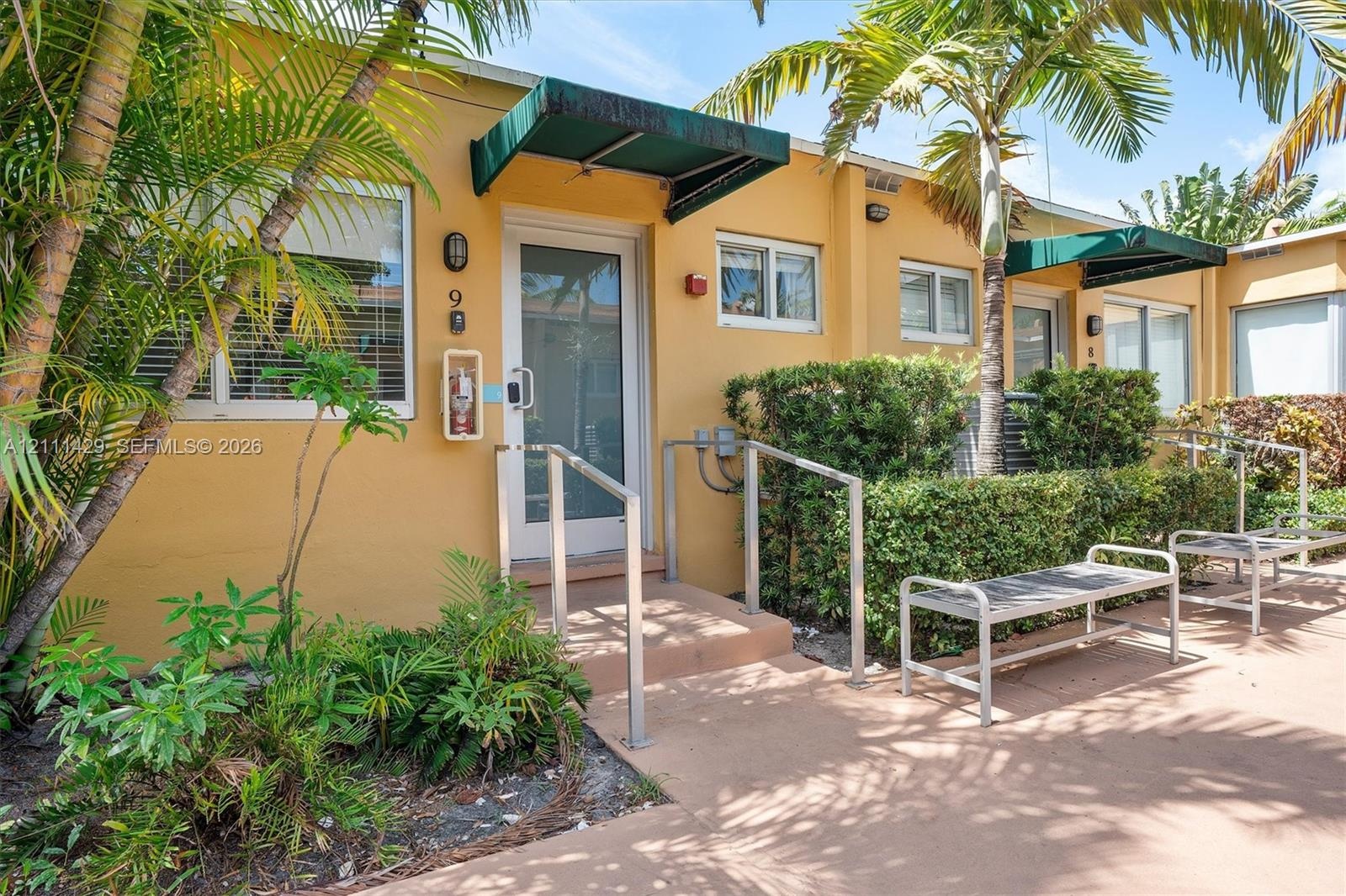 Stucco exterior featuring dual-pane windows, metal door awnings, concrete walkway, and built-in metal handrails
