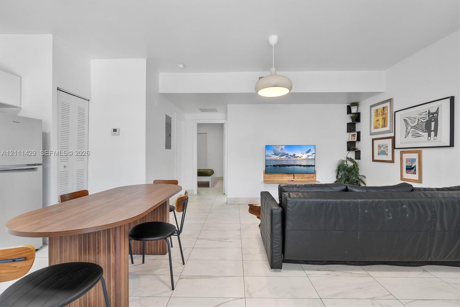 Open floor plan featuring large-format tile flooring, a modern dome-style pendant light, and built-in corner shelving