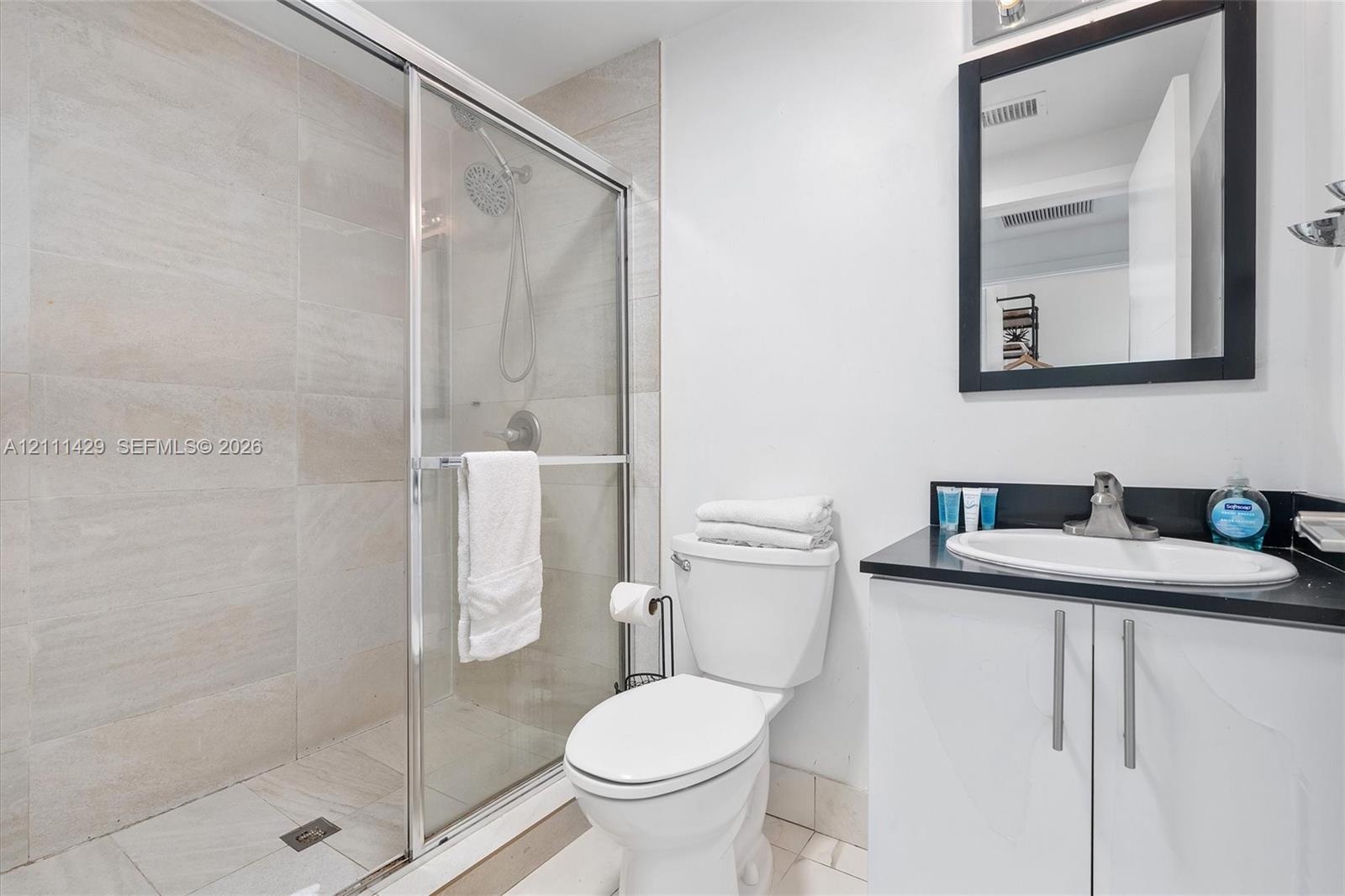 Bathroom featuring a walk-in shower with glass enclosure and large-format tile surround, vanity with dark countertop, integrated sink, and wall-mounte