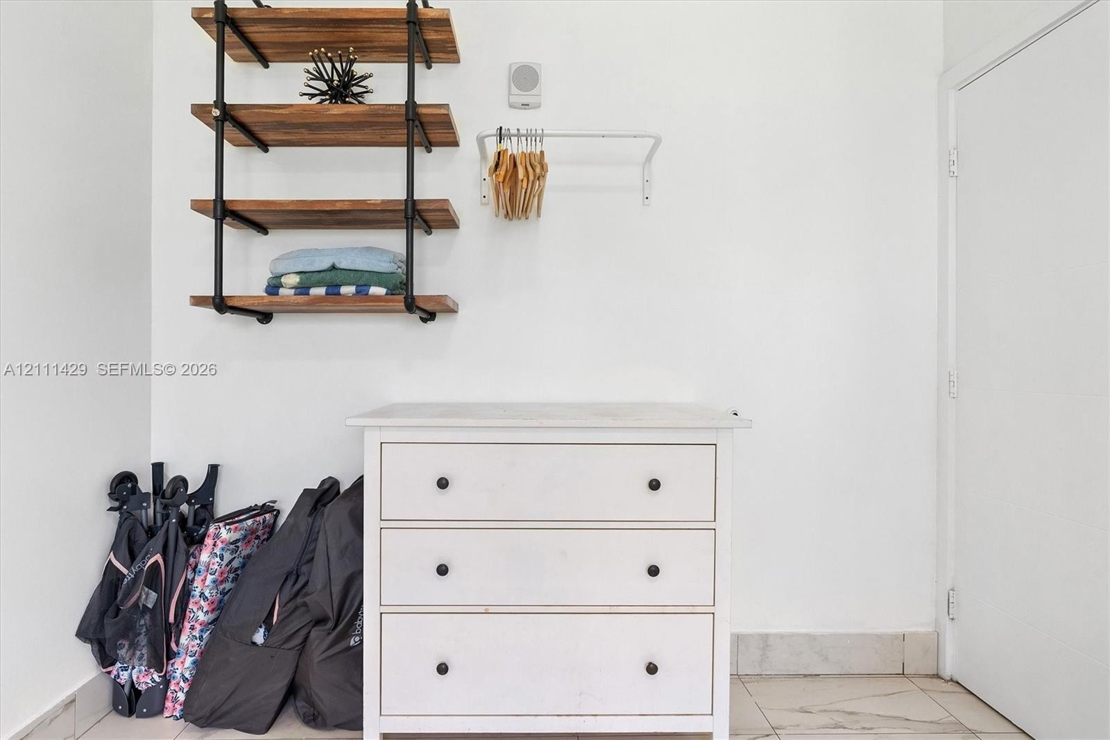 Wall-mounted industrial-style shelving featuring wood-finish tiers and matte black metal piping, white cabinetry, and a wall-mounted metal garment rai