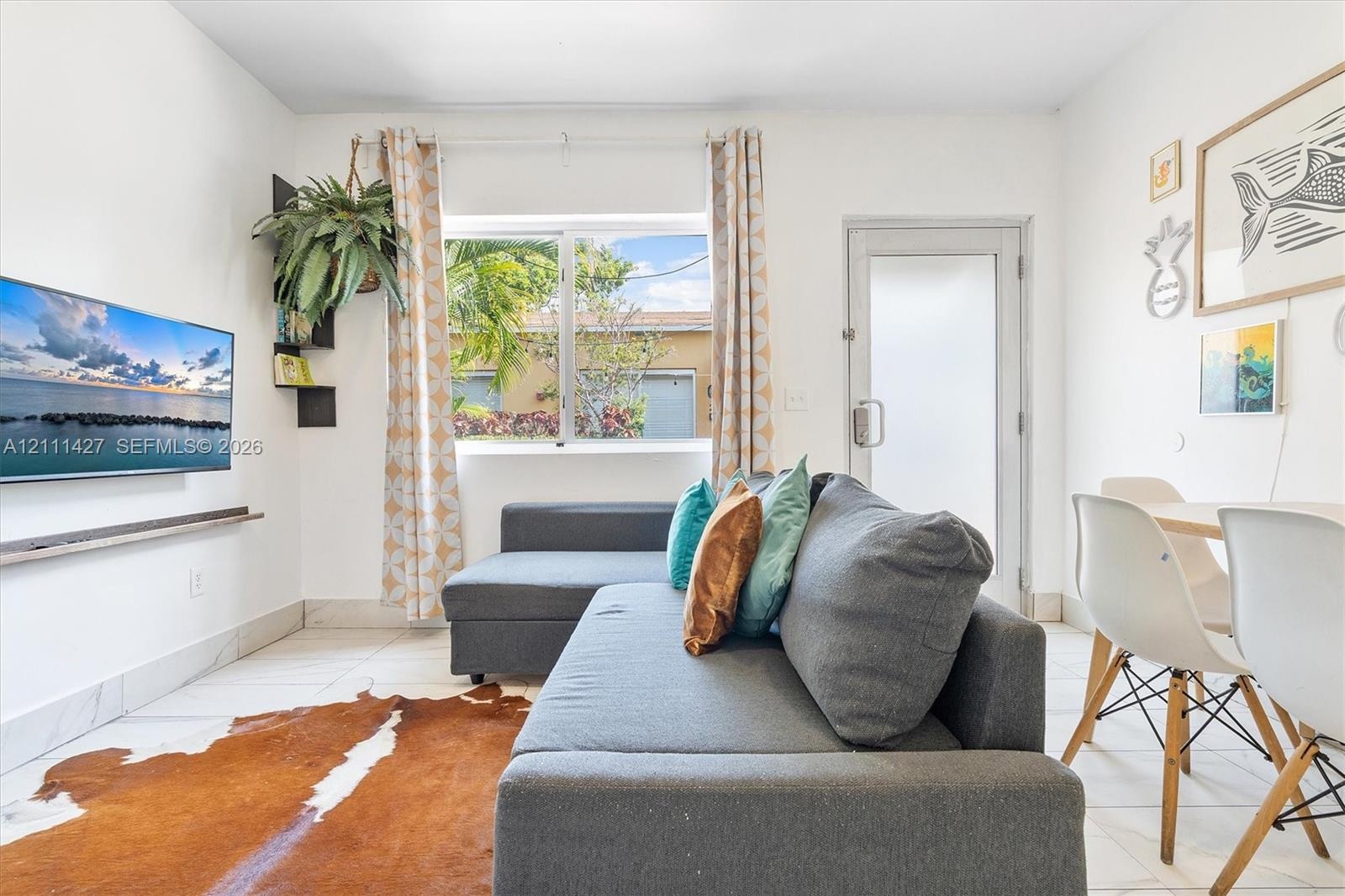 Living area featuring white tile flooring, a wall-mounted floating shelf, and a glass-paneled exterior door