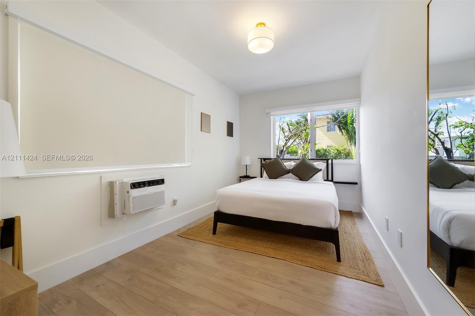 Room featuring wood-finish flooring, a wall-mounted climate control unit, a recessed window, a flush-mount globe light fixture, and a full-length wall