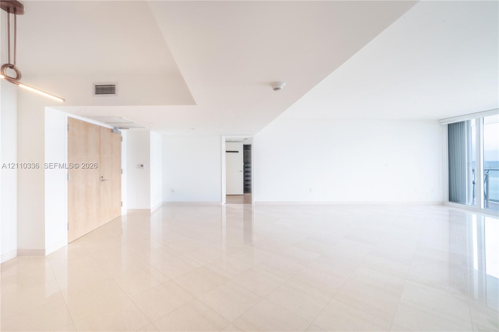 Open-concept interior featuring light-toned tile flooring, floor-to-ceiling windows, natural finish wood doors, and a contemporary linear pendant ligh
