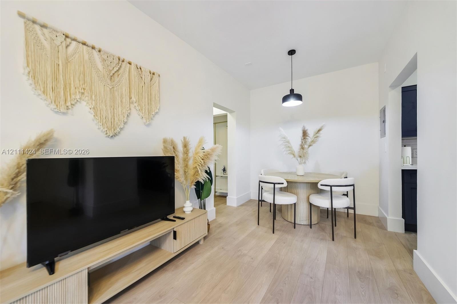 Neutral interior space featuring wood-finish flooring, crisp white walls, and a contemporary matte black pendant light fixture